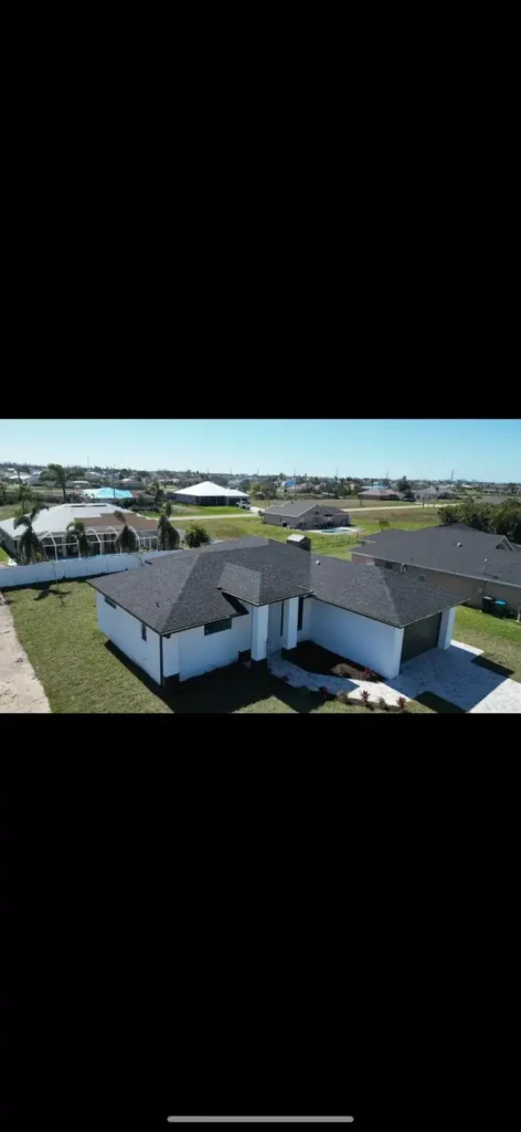 New aerial angle of house with black shingle roof and pool construction.