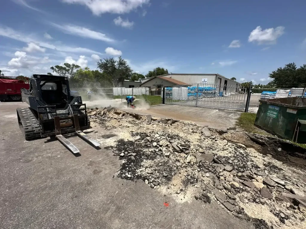 Workers removing a concrete slab with heavy machinery.