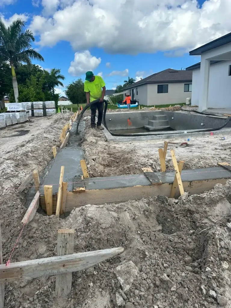 Worker pouring concrete during pool renovation project.