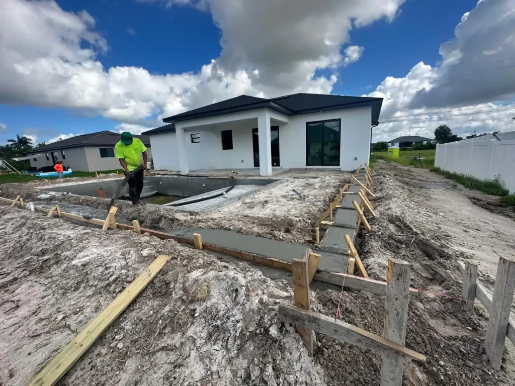 Worker pouring concrete for pool foundation with visible wooden supports.