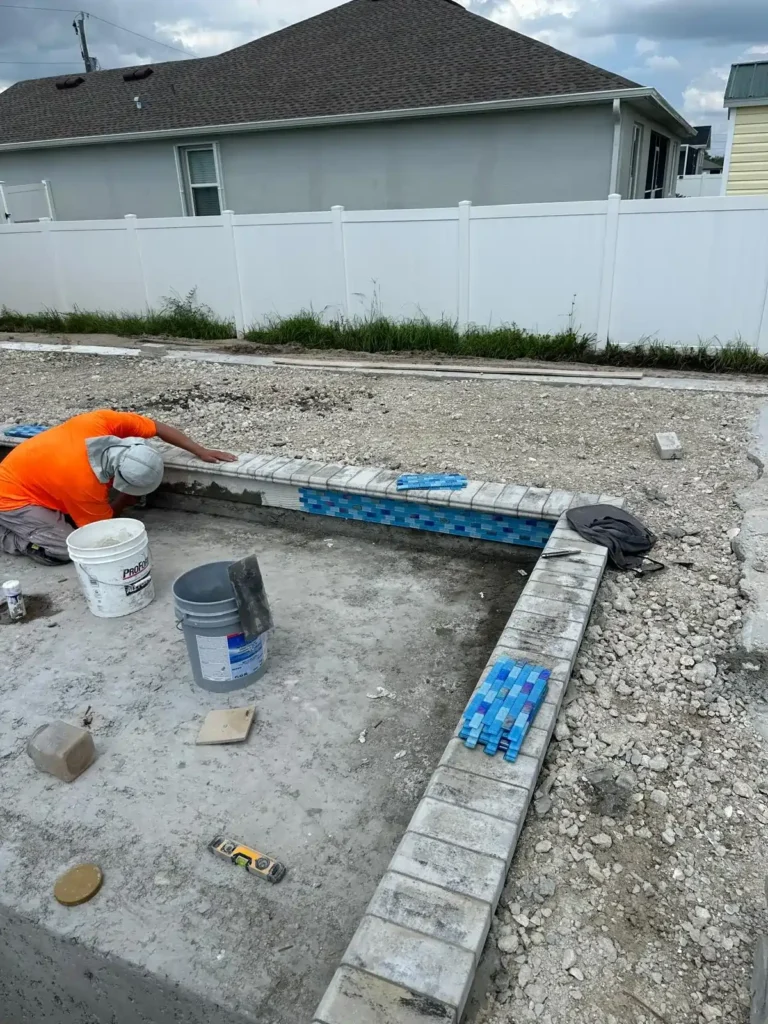 Worker installing tile around the edge of a swimming pool.