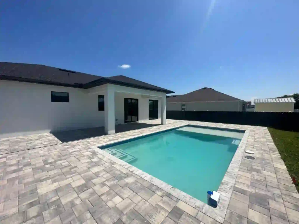 Backyard pool area of a modern home with a tiled patio and shaded seating area.