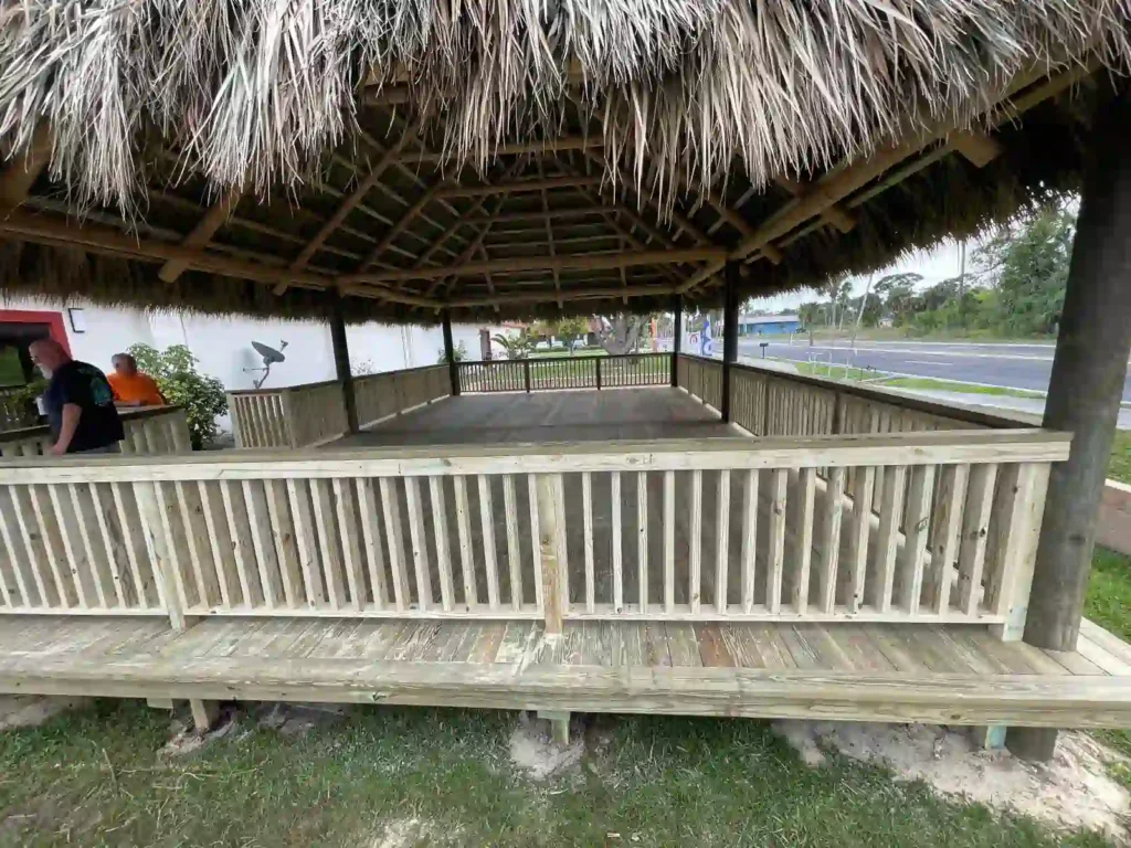 Large tiki hut with a wooden frame and surrounding fence.