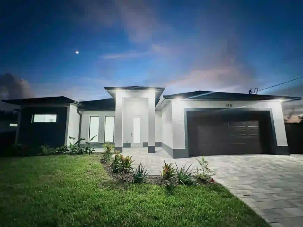 Modern home entrance at night with well-lit pathway and stucco exterior.