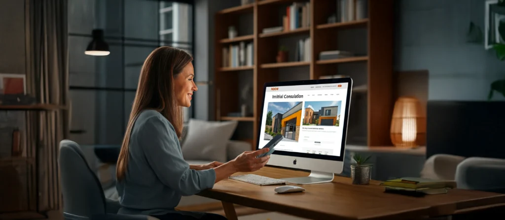 Customer engaged in a phone consultation with a construction company, viewing their website on a computer in a home office.